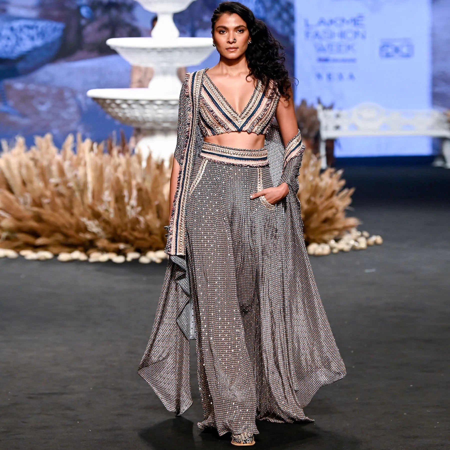 TEXTURED CROP TOP TEAMED WITH EMBELLISHED PINK BUTTI PRINT BOX PLEAT PANTS WITH HIGHLIGHTED CAPE